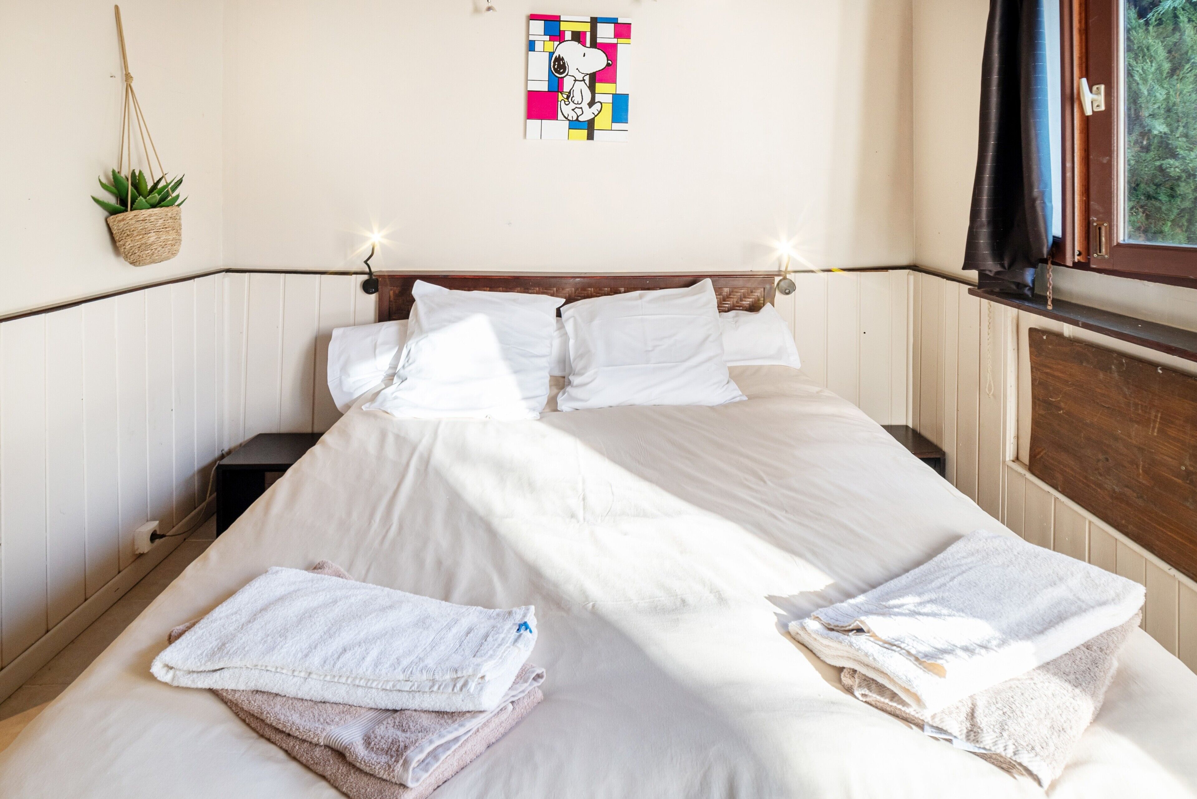 Ein Bett mit weißer Bettwäsche, eine Wandpflanze und ein farbenfrohes Kunstwerk.