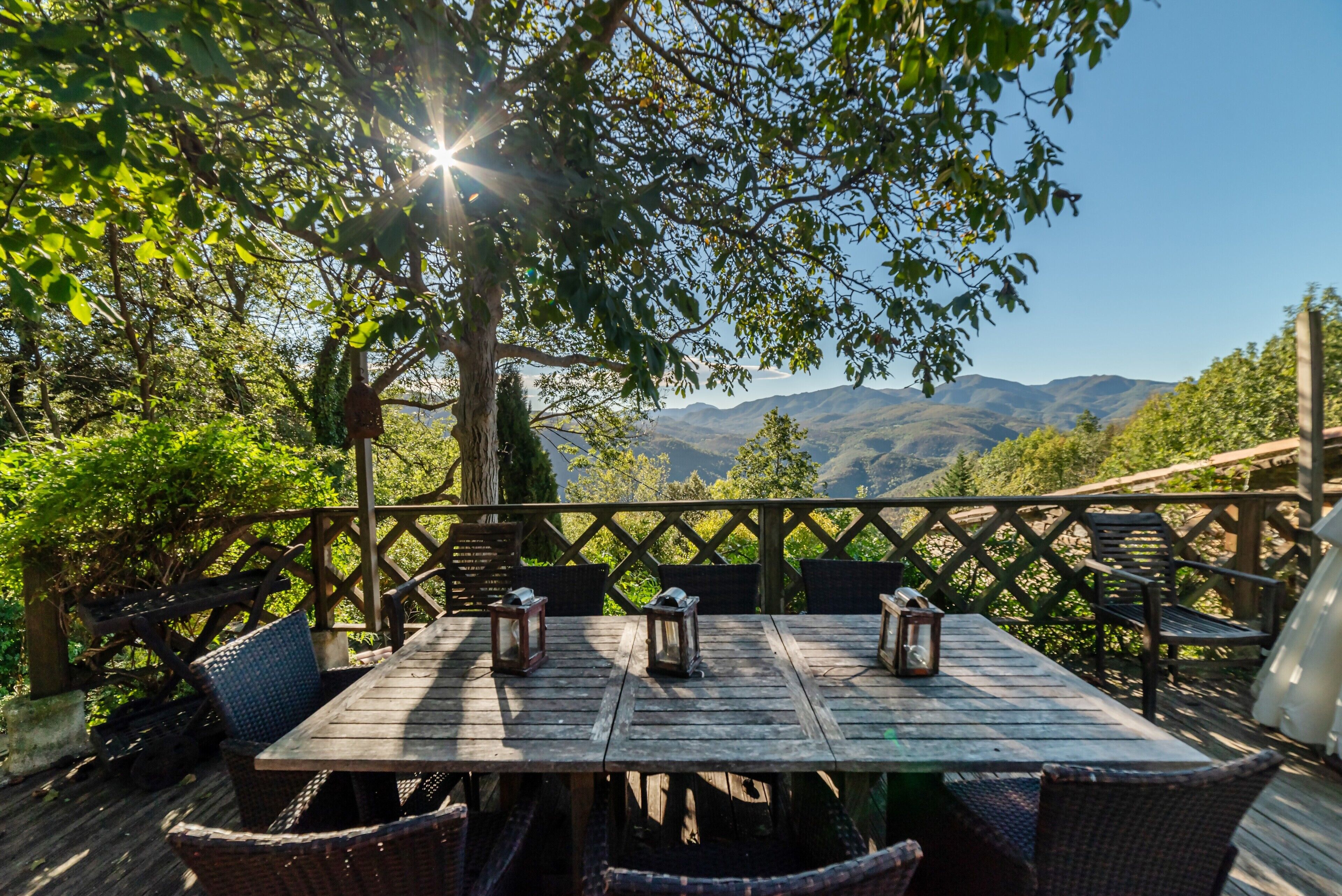 Una terraza de madera con una mesa y sillas, rodeada por una valla de madera, con vistas a un paisaje montañoso.