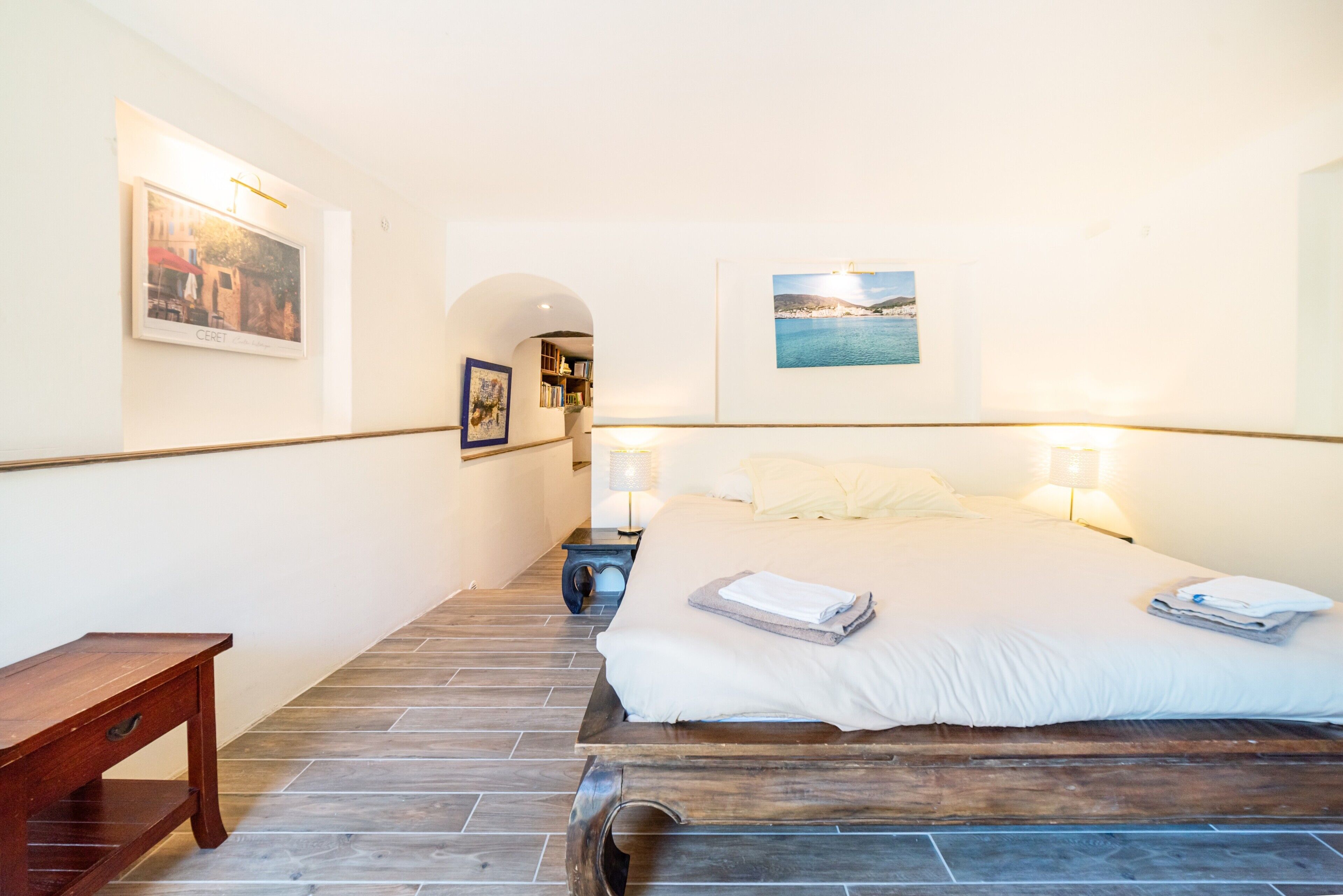 Una habitación de hotel con una cama, una mesita de noche, un banco de madera y dos lámparas fijadas a la pared.