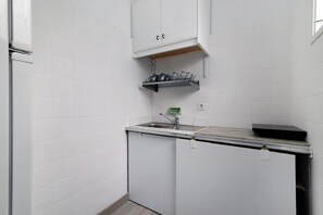 A small kitchenette with a sink, a shelf above the sink, and a cabinet below.