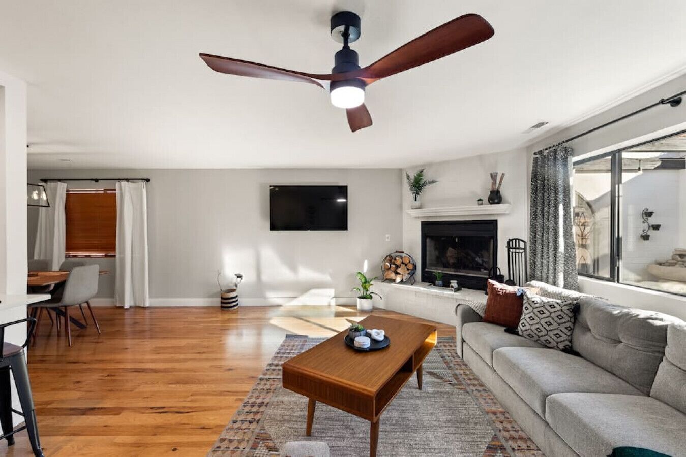 A modern living room with a wooden floor, a ceiling fan, a flat-screen TV, a fireplace, and a sofa.