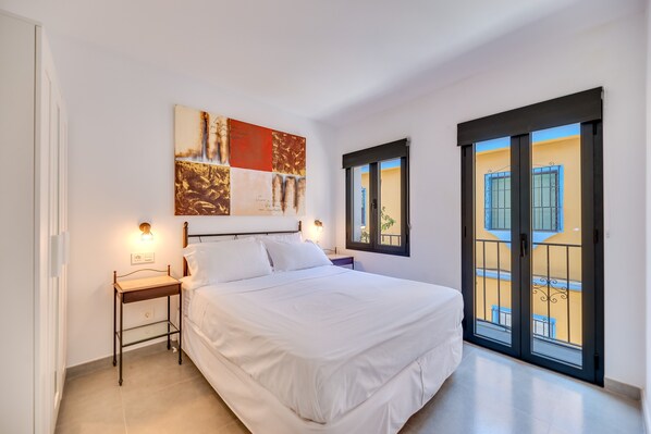 Une chambre à coucher comprenant un lit, des tables de chevet, une œuvre d’art accrochée au mur et un balcon doté d’une balustrade.