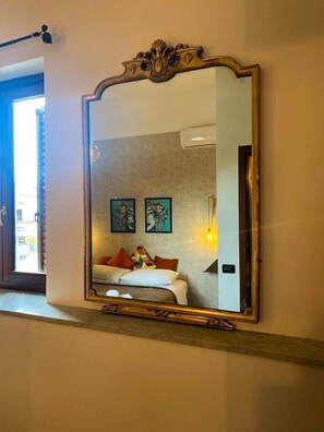 Une chambre avec un grand miroir, un lit avec des oreillers et deux œuvres d’art accrochées au mur.