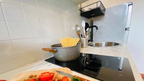 Una cocina con una olla de espagueti, una tabla de cortar con tomates y almendras, un cuchillo y un fregadero.