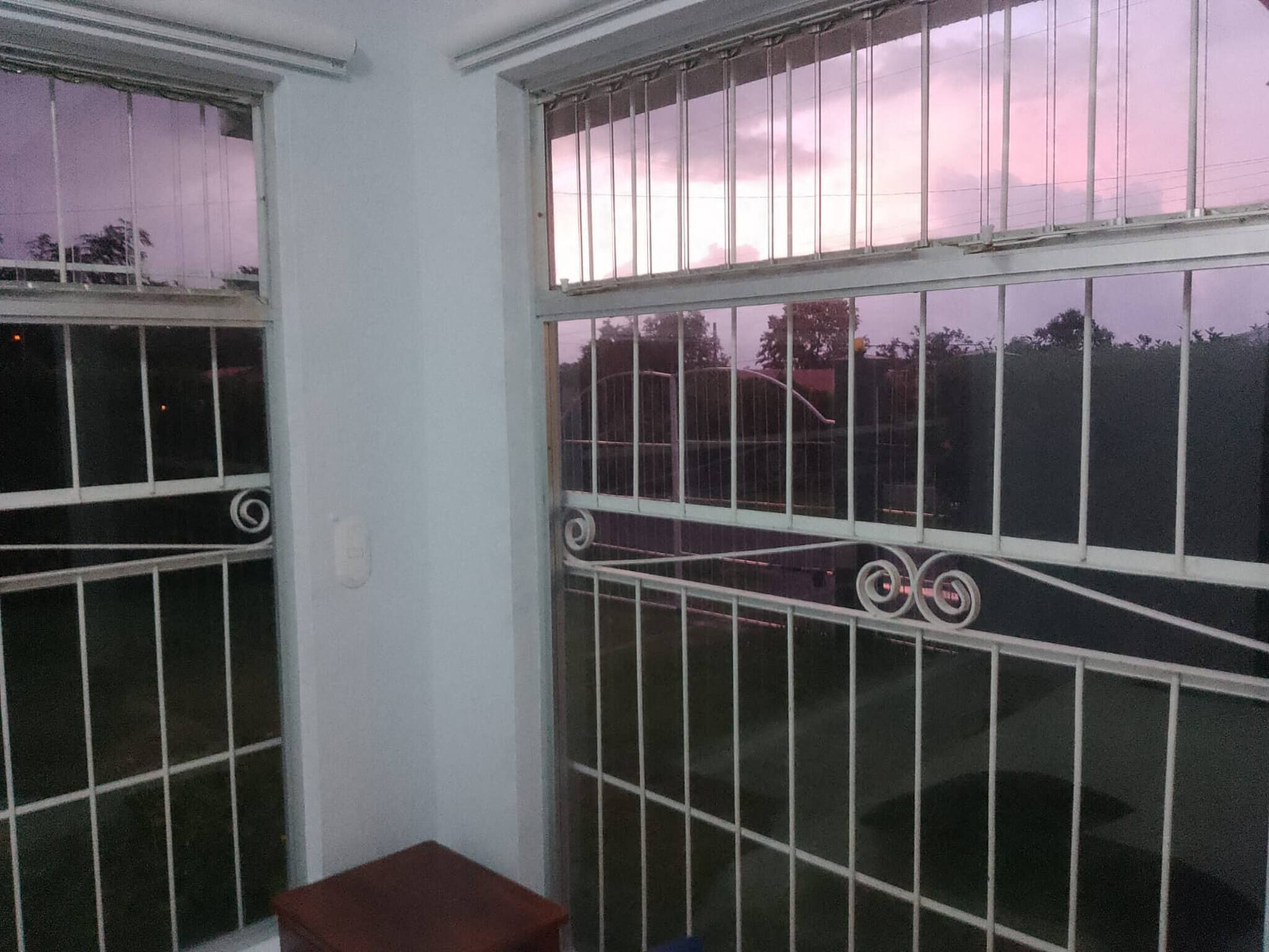Una habitación con ventanas de rejas, un taburete de madera y una barandilla de metal.