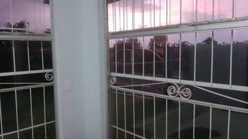 Una habitación con ventanas de rejas, un taburete de madera y una barandilla de metal.