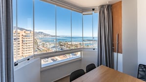 A room with a large window offering a view of a coastal cityscape, a wooden table, and a chair.