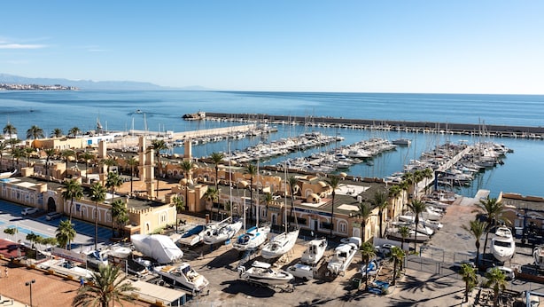 A marina with boats docked, a pier extending into the water, and a building with a dome structure.