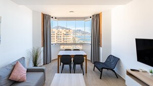 A modern living room with a dining area, a sofa, a TV, and a large window with a city view.