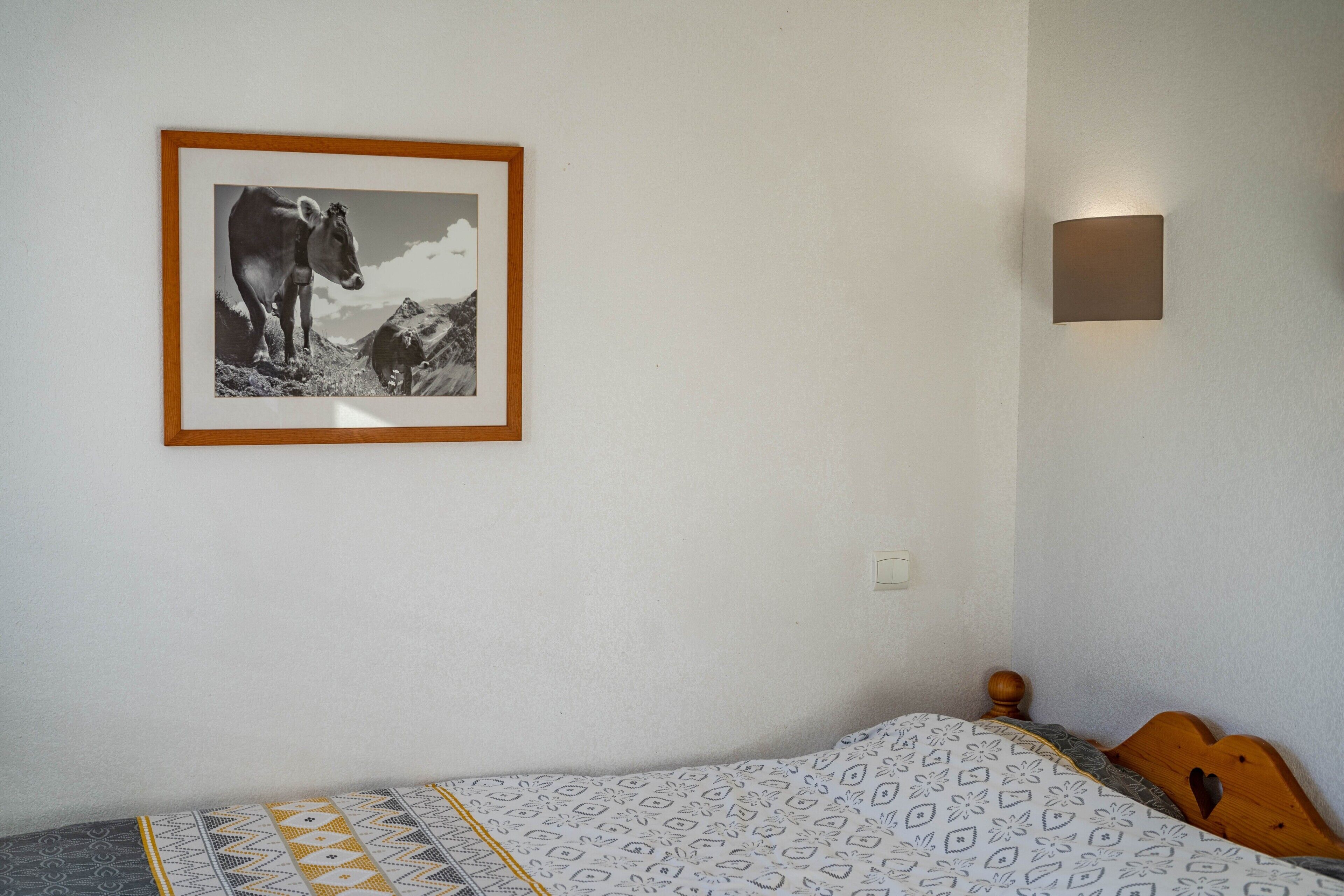 Ein Schlafzimmer mit einem Bett, einem gerahmten Bild an der Wand und einer Wandleuchte.