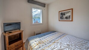 Une chambre à coucher avec un lit, un téléviseur posé sur un meuble en bois, une fenêtre donnant sur un paysage agréable et un tableau encadré accroché au mur.