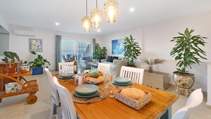 Un coin repas avec une table en bois dressée pour quatre personnes, entourée de chaises blanches, donnant sur l’espace de vie.