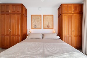 A bedroom with a large bed, wooden wardrobe, two wall-mounted paintings, and bedside lamps.