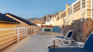 Un espace piscine aménagé sur le toit, avec des chaises longues, une piscine et une vue sur les montagnes.