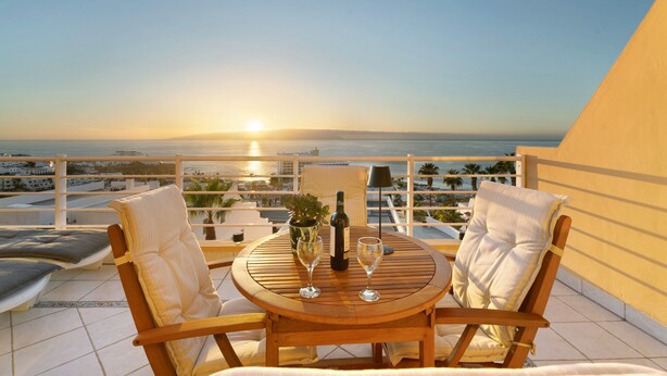 Un balcon avec une table, deux chaises, une bouteille de vin et un verre.
