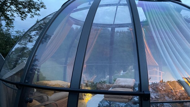 Una estructura de cúpula transparente con un área de asientos acolchada y una silla en su interior.