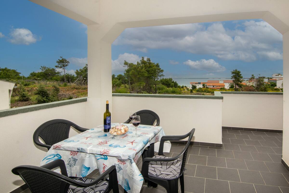 A balcony with a table set for two, a bottle of wine, and a glass of red wine.