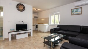 A modern living room with a glass coffee table, a black sofa, a TV on a white stand, and a kitchen in the background.