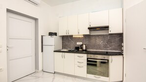 A modern kitchen with white cabinets, a black countertop, and a marble backsplash.