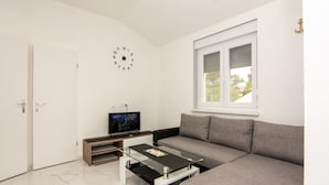 A modern living room with a sofa, a glass coffee table, a television, and a clock on the wall.