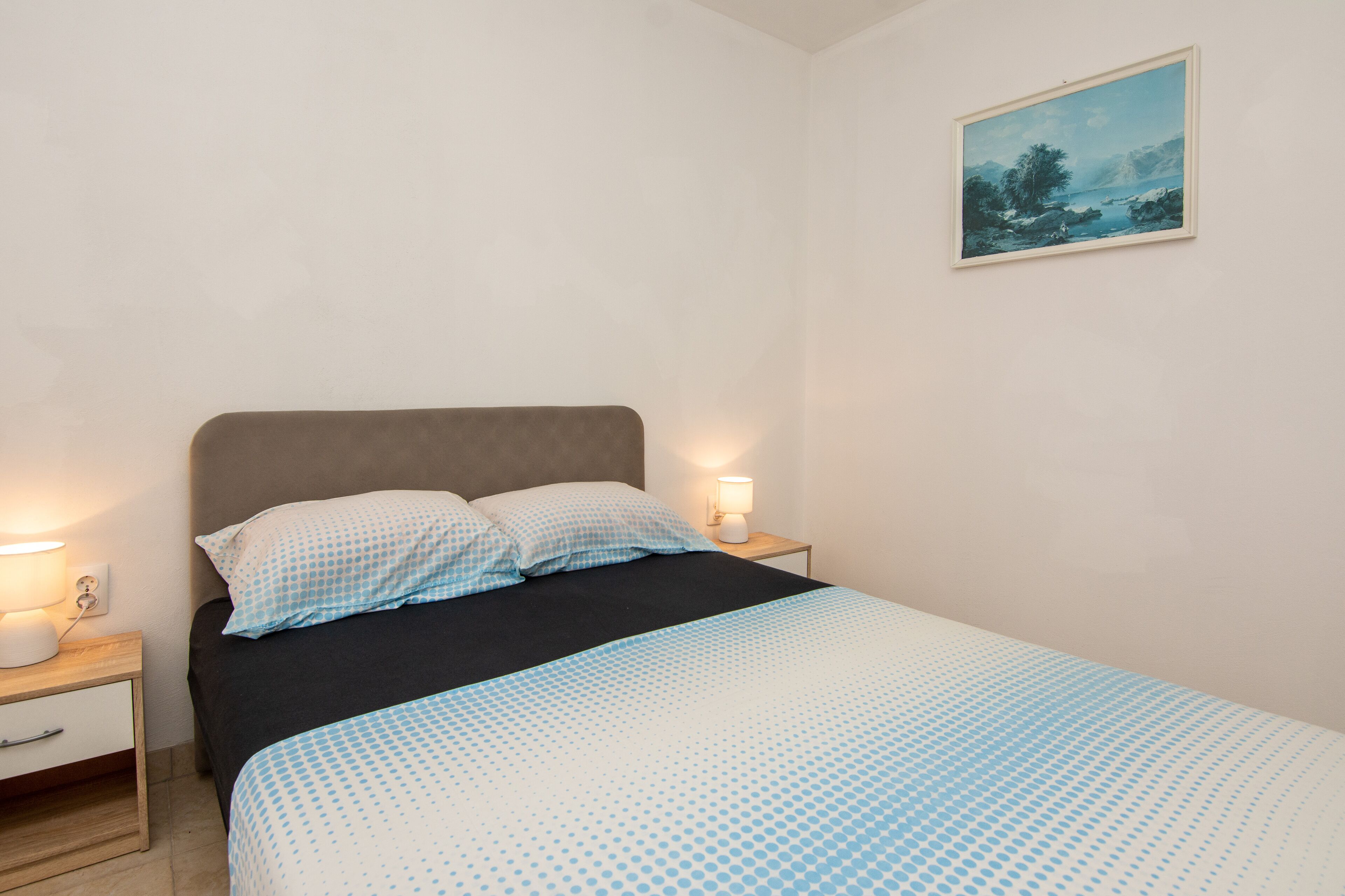 Une chambre à coucher avec un lit, deux tables de chevet, une lampe de chevet et un tableau au mur.