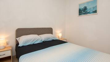 A bedroom with a bed, two bedside tables, a night lamp, and a painting on the wall.