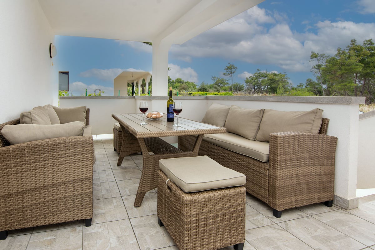 A patio area with wicker furniture, a table, and a bottle of wine.