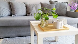 Un salon moderne avec un canapé gris, une table basse blanche et un vase contenant des plantes vertes.