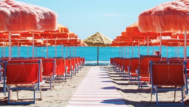Una playa con filas de sillas rojas de jardín y sombrillas de paja, que dan al agua.