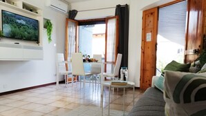 Una sala de estar moderna con un televisor de pantalla plana, un comedor con mesa y sillas, y un ventanal con cortinas.