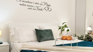 Una cama bien hecha con ropa de cama blanca y turquesa, un cojín verde y una mesita de noche con una lámpara y una planta.