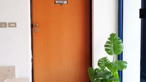 A wooden door with a sign, a potted plant, and a doormat. - HoliHome_Nobil Villani (Tortoreto Lido)