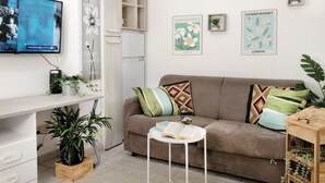 A living room with a sofa, a small side table, a TV mounted on the wall, and framed pictures of flowers. - HoliHome_Nobil Villani (Tortoreto Lido)