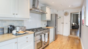 A modern kitchen with white cabinets, a stainless steel stove, and a refrigerator. - Cobblers Cottage (Beaumaris)