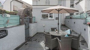 A small outdoor seating area with a round table and wicker chairs, a heart-shaped door knocker, and a sign reading "Welcome to our Beer Garden." - Cobblers Cottage (Beaumaris)