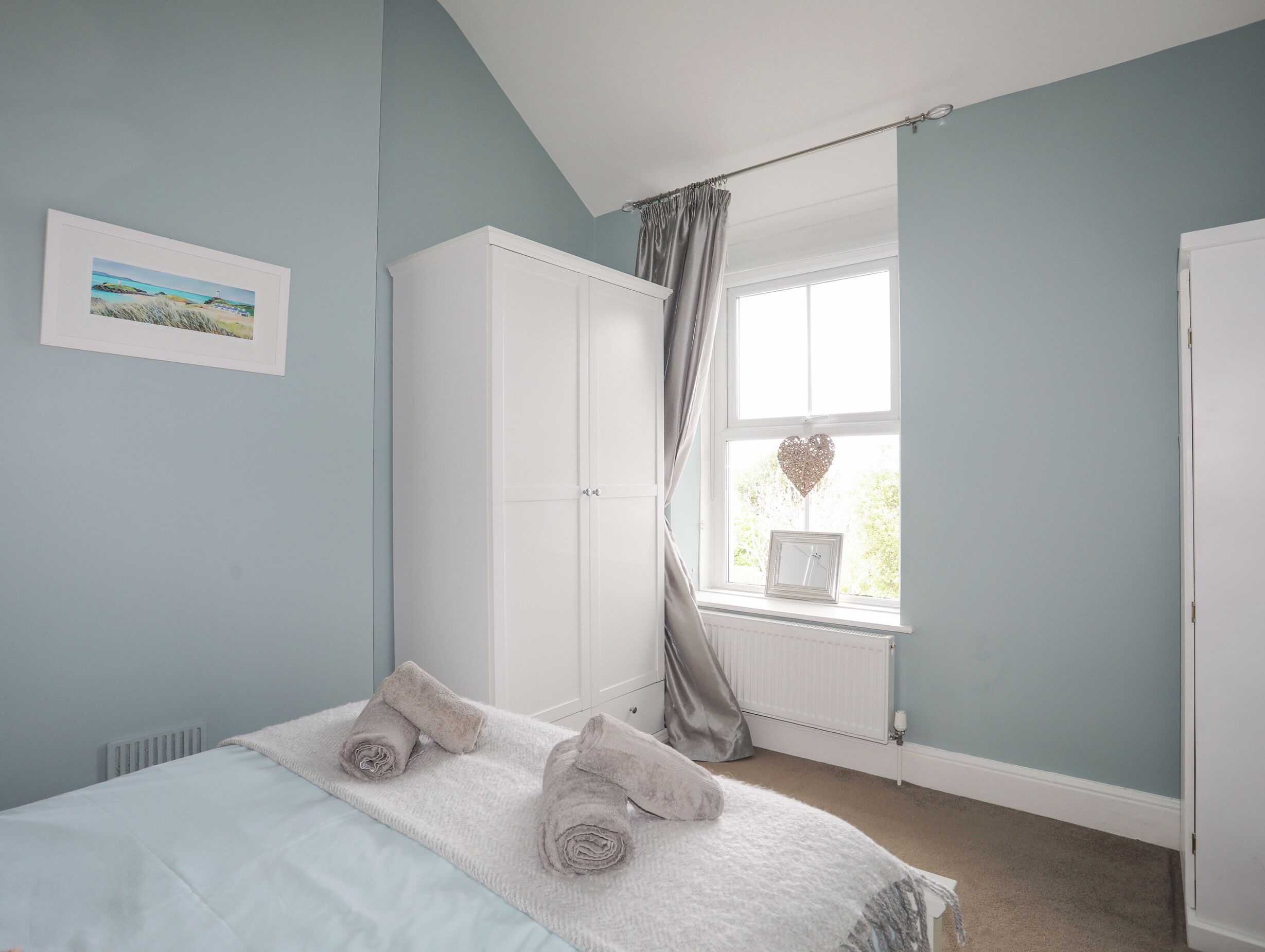 A bedroom with a bed, a wardrobe, a window with curtains, and a framed picture on the wall.