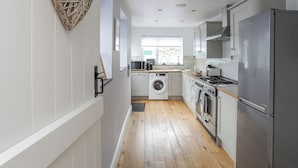 A modern kitchen with a washing machine, oven, and stainless steel refrigerator. - Cobblers Cottage (Beaumaris)