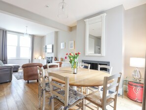 Un salon spacieux avec une table à manger en bois, des chaises blanches, un canapé et une cheminée.