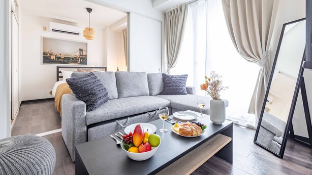 A modern living room with a grey sofa, a coffee table with fruit and pastries, and a dining area with a white table and chairs. - STAY 1ST (Osaka)