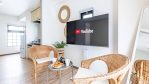 A modern living room with wicker furniture, a flat-screen TV, and a small table with a plant and croissants. - STAY 1ST (Osaka)