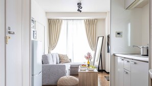 A modern kitchen with white cabinets, a wooden countertop, and a dining area with a grey sofa and ottoman. - STAY 1ST (Osaka)