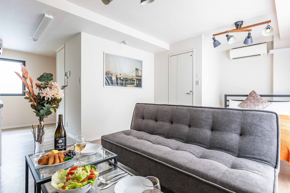 A modern living room with a grey sofa, a glass coffee table, and a dining area with a plate of food and a bottle of wine.