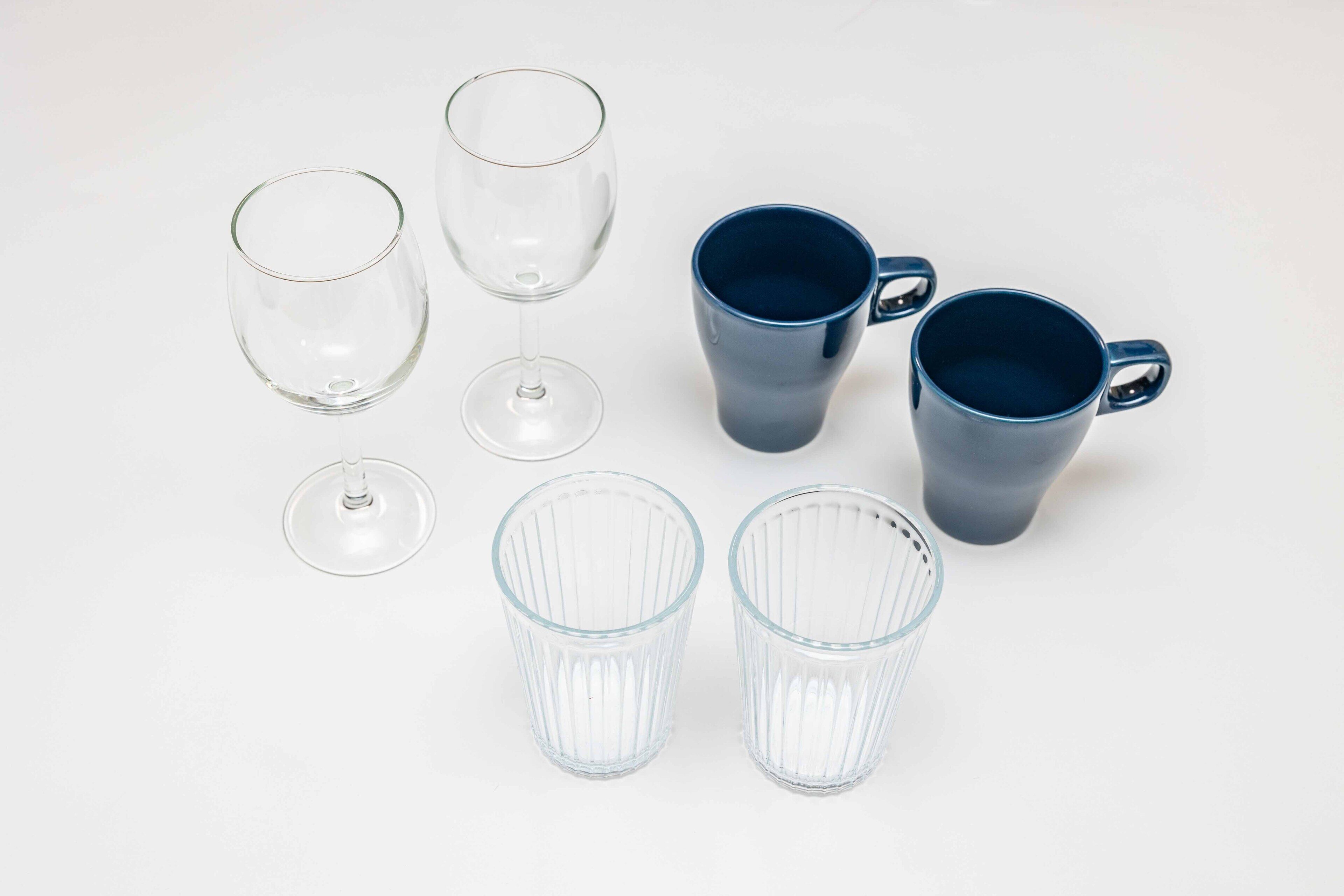 A collection of clear and blue glassware, including wine glasses and mugs, arranged on a white surface.