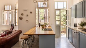 Eine moderne Küche mit einer zentralen Kochinsel, ein Essbereich mit einer Ledersofa und Blick durch offene Fenster.