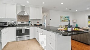 Cocina moderna con armarios blancos, electrodomésticos de acero inoxidable y una isla central con una botella de vino y copas.