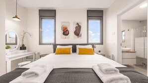 Ein modernes Hotelzimmer mit einem großen Bett, zwei Fenstern, einem Schreibtisch und einem durch eine offene Tür einsehbaren Badezimmer.