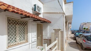 A narrow street with a white building, a tiled roof, a small table with chairs, and parked cars. - 3550 Casa Cleopatra by Barbarhouse (Porto Cesareo)