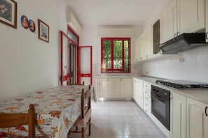 Una cocina compacta con una mesa de comedor, armarios y un ventanal con marcos rojos.