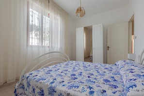 Un dormitorio con cama, una silla, una ventana con cortinas y una puerta.