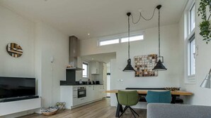 Ein modernes Wohnzimmer mit einem grauen Sofa, einem Holztisch und einem Essbereich mit einem grünen Stuhl.